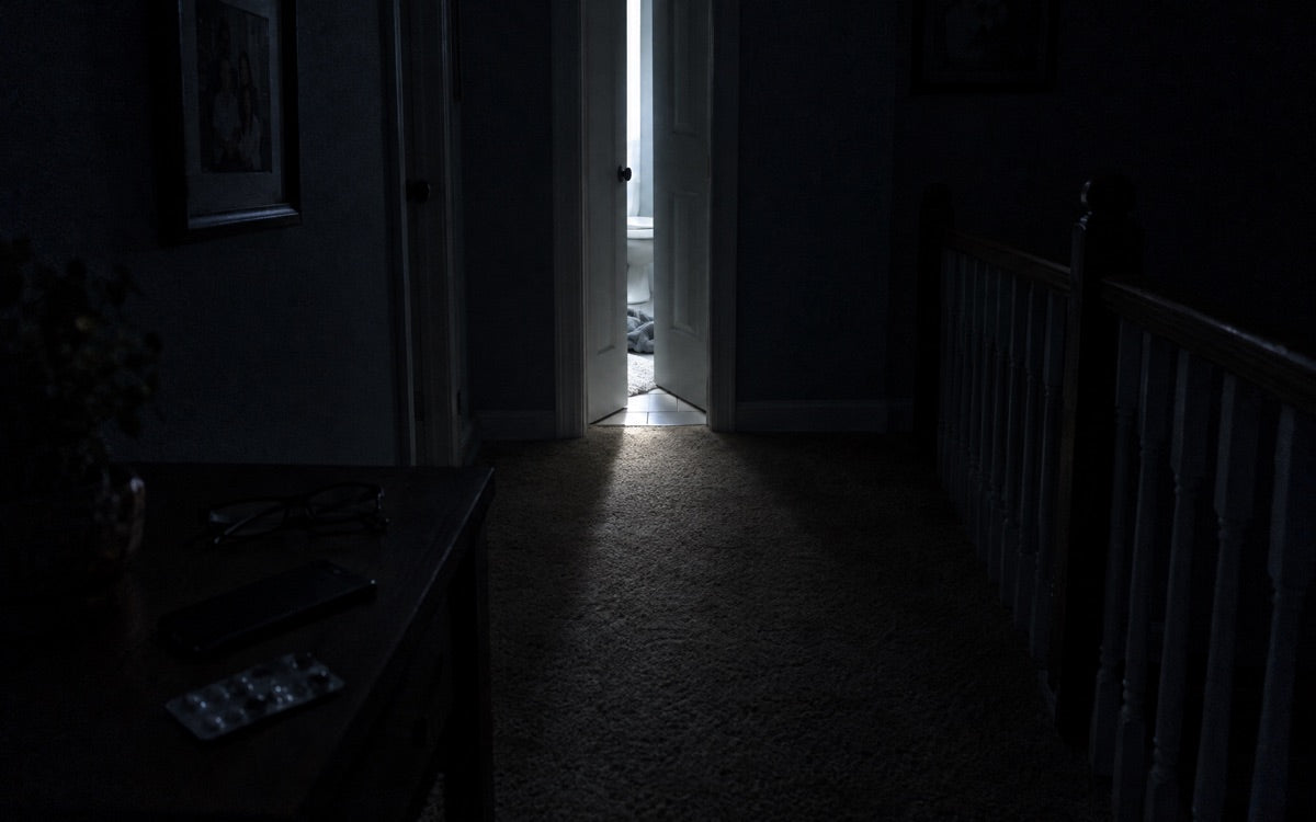 A dim hallway at 2:47 a.m.: bathroom door cracked, light on tile, no face, no body