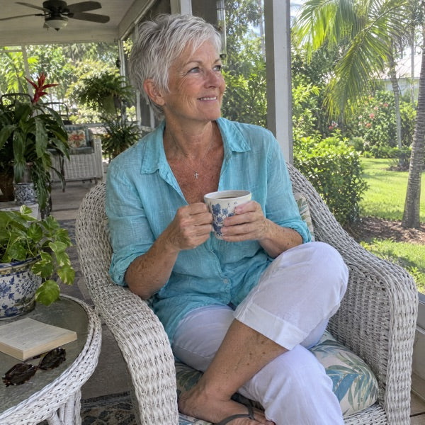 A woman in her sixties on a porch, mid-morning, a cup, no lemon-water aesthetic